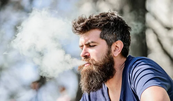 Man long beard relaxed with smoking habit. Man with beard breathe out smoke. Clouds of flavored smoke. Stress relief concept. Bearded man smoking vape. Smoking electronic cigarette. Smoking device