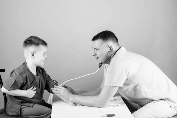 Buen equipo. niño feliz con padre con estetoscopio. Asistente de laboratorio de enfermería. médico de familia. padre e hijo en uniforme médico. medicina y salud. Un niño pequeño con papá jugando. Carrera futura — Foto de Stock