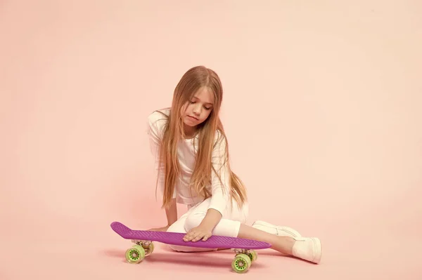 彼女のペニーボードを愛する。ピンクの背景にボードデッキに手を置く小さな女の子。バイオレットペニーボードと愛らしい小さなスケーター。スケートボードでトリックを実行する — ストック写真