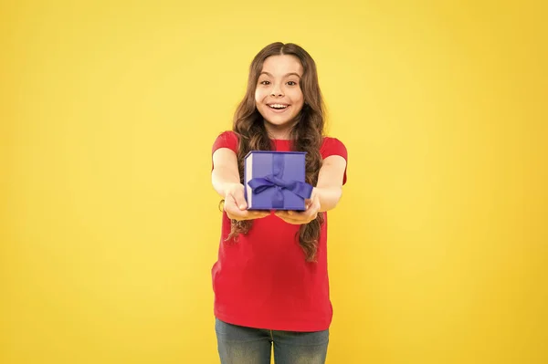 Gift giving gör henne lycklig. Bedårande liten flicka som ger blå presentbox på gul bakgrund. Söta små barn njuta av att ge gåvan. Gåva att ge tillfälle — Stockfoto
