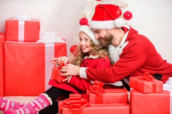 今年は子供の休日を特別なものにしてください。子供へのクリスマスプレゼント。サンタの衣装のお父さんは娘のかわいい子供に贈り物を与えます。幸せな子供時代。クリスマスの家族の休日。クリスマスの父の概念 — ストック写真