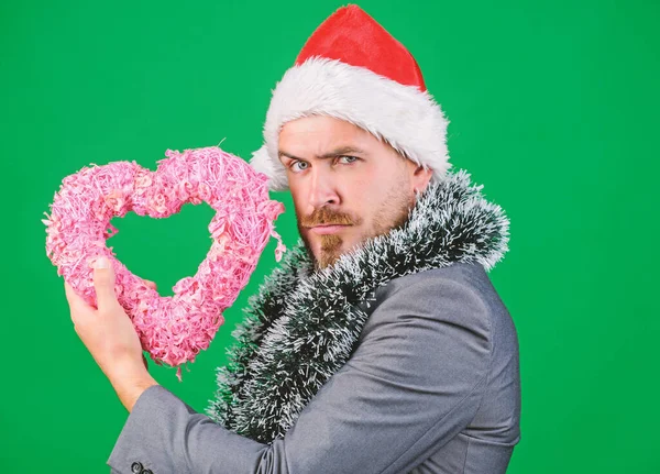 Merry christmas and happy new year. Hipster hold heart symbol of love. Bring love to family holiday. Spread love around. Man in love happy wear santa hat celebrate christmas green background