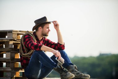 Bırak ata binsin. Vahşi batı rodeosu. Şapkalı düşünceli adam viski içiyor. Batı kovboyu. Klasik tarz adam. Vahşi Batı eski kovboy. Kement ipli bir kovboy. Batı. Çiftlikte kareli gömlek