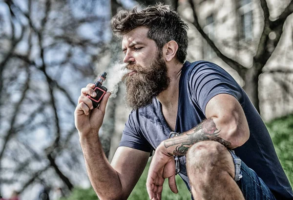 Bearded man smoking vape. Smoking electronic cigarette. Smoking device. Man long beard relaxed with smoking habit. Man with beard breathe out smoke. Clouds of flavored smoke. Stress relief concept