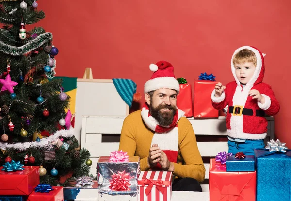 Santa y pequeño asistente entre cajas de regalo cerca del árbol de Navidad. — Foto de Stock