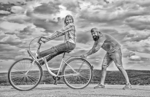 Woman rides bicycle sky background. Man helps keep balance and ride bike. How to learn to ride bike as adult. Girl cycling while boyfriend support her. Cycling technique. Learn cycling with support