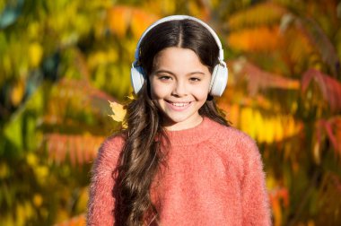 Sonbahar gününün tadını çıkar. Güzel şarkılarla sonbahar yürüyüşleri. Çocuklar için eğitici ve indirilebilir sesli kitaplar. Küçük kız kulaklıklarla sonbahar ağacının yanında dinleniyor. Sonbahar havası için müzik. Dinleyen şarkı