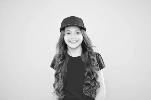 Hermoso Maximus. niña pequeña con el pelo largo. chica cool con el pelo largo y rizado. Moda infantil. chica feliz con gorra hipster de moda. niño hipster sobre fondo amarillo. Feliz infancia. belleza y moda — Foto de Stock