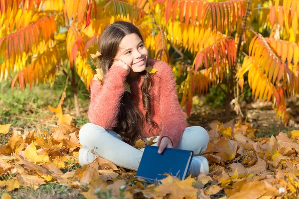 Bringing school into nature. Cute primary school child with book sit on yellow leaves. Happy little girl back to school in autumn. Time after school. September 1