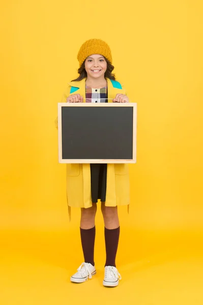 Informatieverstrekking. Gelukkig meisje houden blanco schoolbord voor informatie gele achtergrond. Klein kind glimlach met netjes schoolbord voor schoolinformatie. Informatiebord, kopieerruimte — Stockfoto