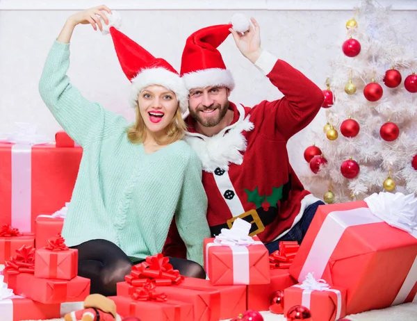 Veselá rodina slaví Vánoce. Vánoční dárek. Pár nosit klobouky jako Santa Claus vánoční strom pozadí. Zamilovaný pár si užije vánoční oslavu. Je snadné šířit kolem sebe štěstí — Stock fotografie
