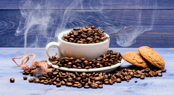 Coffee for inspiration and energy charge. Cup full coffee brown roasted beans white clouds of smoke blue wooden background. Degree of roasting grain. Cafe drinks menu. Fresh roasted coffee beans
