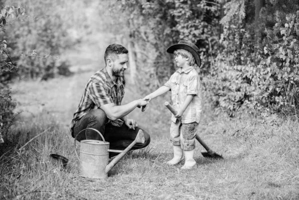 父亲和在牧场牛仔帽的儿子。快乐地球日。家庭树护理。浇水罐，锅铲。花园设备。生态农场。小男孩在农场帮助父亲。为每个人提供最好的服务 — 图库照片