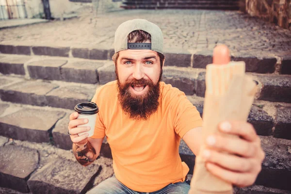 Refeição que sabe bem. Homem barbudo comendo alimentos insalubres durante o descanso e a pausa para refeições. Hipster comendo refeição de cachorro quente nas escadas ao ar livre. caucasiano cara gosta de comer takeaway refeição — Fotografia de Stock