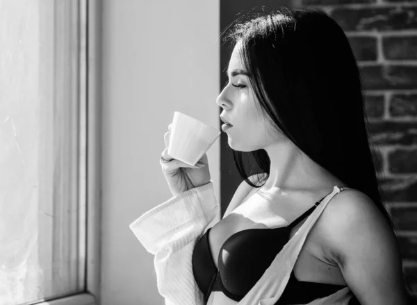 Ragazza seni sexy bere caffè vicino davanzale della finestra. Intimo femminile attraente rilassante a casa. E 'ora del caffe'. Ma prima il caffè. Tranquillità e pace. Sorso di cappuccino cremoso. Rituale del mattino — Foto Stock