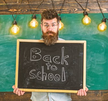 Okul yılı konsepti. Şaşırmış surat ifadesindeki öğretmen okula geri dönen bir tahtanın üzerinde duruyor. Sakallı adam öğrencileri karşılıyor, arka planda kara tahta var. Öğretmen tebeşir deliğinden dikizliyor.