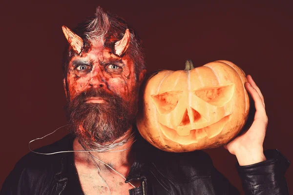 Demon with horns and serious face holds jack o lantern. — Stock Photo, Image