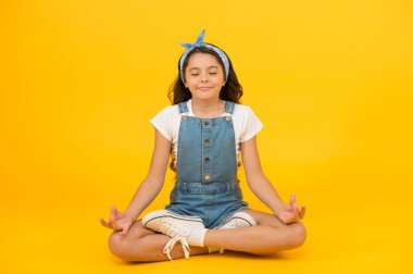 Rahatla ve rahatla. Küçük kız sarı arka planda yoga pozisyonunda oturuyor. Küçük çocuk yoga eğitiminin tadını çıkarıyor. Yoga meditasyonu. Meditasyon ya da yoga