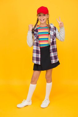 At kuyruklu hippi. Küçük mutlu hipster beyzbol şapkası sarı arka plan giyer. Havalı görünüşlü sevimli hippi gülüşü. Hippi tarzında sevimli bir çocuk.