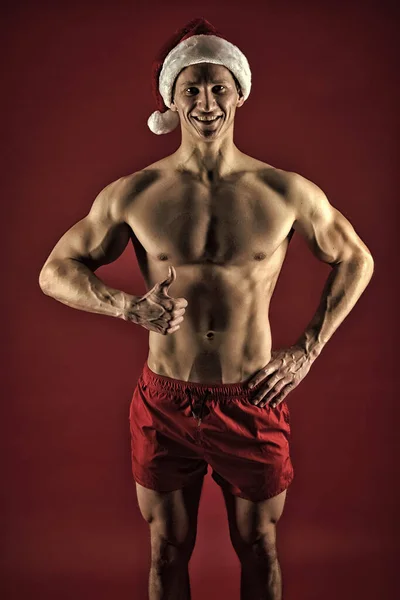 Atleta uomo indossare cappello di Babbo Natale e pantaloncini rossi. Sexy macho atletico in cappello di Babbo Natale. Se tu fossi una ragazzaccia. Macho sexy busto muscolare posa con fiducia. Babbo Natale non viene solo alle brave ragazze — Foto Stock