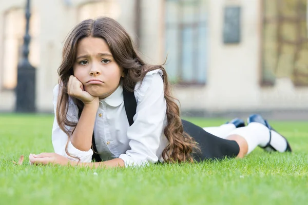 Triste senza un sorriso. Studentessa triste rilassarsi su erba verde. Adorabile bambino con una triste emozione sul viso. Mi sento triste e infelice. Tristezza e depressione. Problemi scolastici — Foto Stock