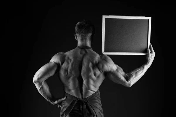 Información culinaria de la escuela. Cook mantenga el tablero de información en una vista trasera de la mano fuerte. Hombre musculoso con pizarra en blanco sobre fondo negro. Lugar de información. Información publicitaria, espacio de copia —  Fotos de Stock