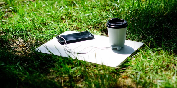 Kaffee zum Mitnehmen. Laptop modernes Smartphone mit Kopfhörer und Kaffeetasse auf grünem Gras. Remote-Job. Kaffeepause im Freien. Sommerferien. Arbeit und Entspannung in der natürlichen Umgebung. seine Kaffeezeit — Stockfoto