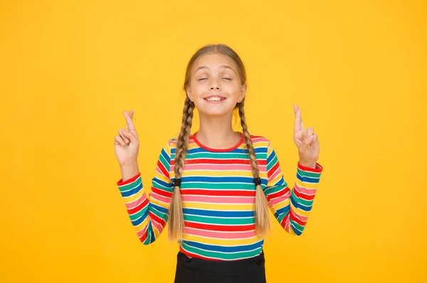 Ich will nicht jinx es. Nettes Kind machen Wunsch gelb Hintergrund. Kleines Kind drückt die Daumen für Glück. Kleines Kind mit langen Zöpfen in lässiger Manier. Ihr Kindertraum — Stockfoto