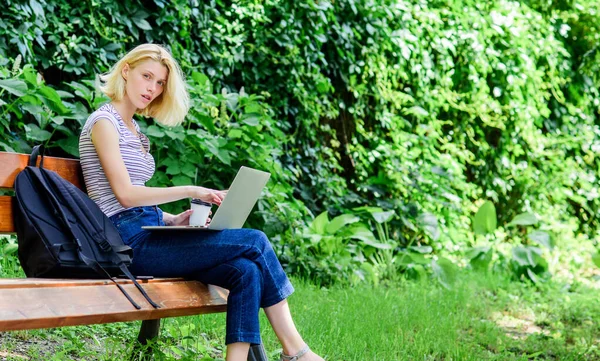Lány imádnivaló diák laptoppal és kávéscsészével ül padon a parkban. Tanulj a szabadban. Női tanulók jegyzetfüzetekkel dolgoznak. Tanulmányi felfedezés. Szörfözök az interneten. Modern diákélet. Rendszeres tanuló — Stock Fotó