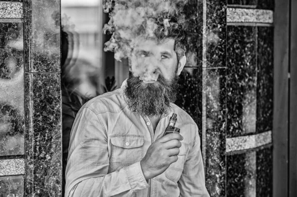 Bearded man smoking vape. Man with beard breathe out smoke. Clouds of flavored smoke. Smoking electronic cigarette. Stress relief concept. Smoking device. Man long beard relaxed with smoking habit