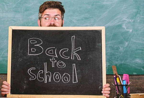 School life full of stress. Teacher or school principal welcomes inscription back to school. Educator hiding behind blackboard. Man scared beginning school year. Teacher peeking out of blackboard