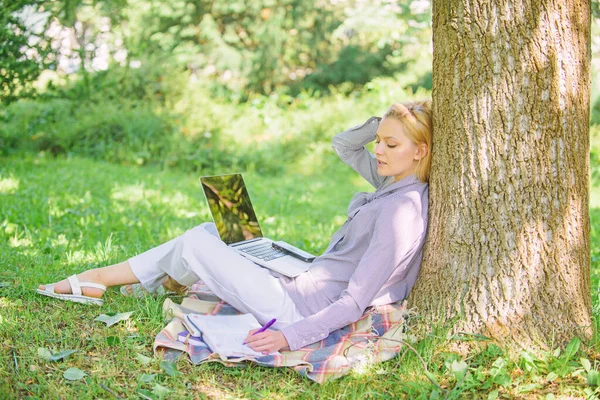 Flicka arbeta med laptop i parken sitta på gräs. Natural Environment Office. Arbete utomhus fördelar. Kvinna med bärbar datorarbete utomhus luta på trädstam. Utbildningsteknik och Internet koncept — Stockfoto