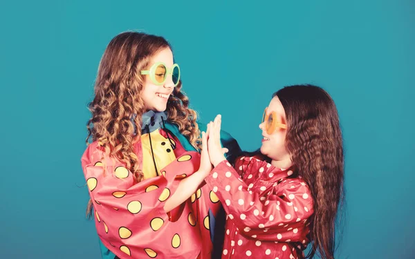 Proteção contra chuva. Arco-íris. moda de outono. crianças hipster alegres, irmandade. a divertir-se. laços familiares. Meninas pequenas em capa de chuva e óculos. meninas pequenas felizes em capa de chuva colorida. Sentimentos puros — Fotografia de Stock