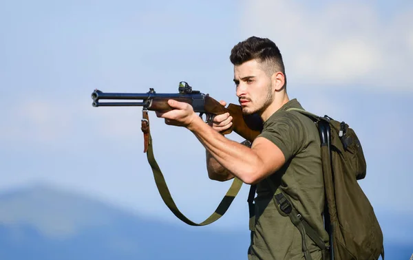 Hunter handsome guy with weapon. Hunter spend leisure hunting. Hunting equipment. Brutal masculine hobby. Man observing nature background. Hunter hold rifle. Safety measures. Natural environment