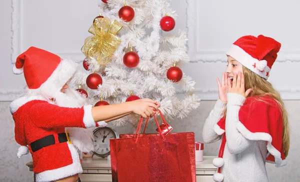 Niño vestido de santa con barba artificial blanca y sombrero rojo dar caja de regalo a la niña. Papá Noel trae regalos. Desempaquetar regalos de Navidad. Feliz navidad. Los niños celebran la Navidad con regalos —  Fotos de Stock