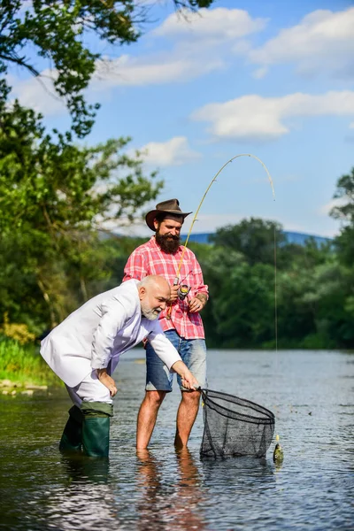 Friends catching fish. Hobby and recreation. Catching fish with soulmate. Bearded man and brutal hipster fishing. Family day. Fishing team. Peace of mind and tranquility. Freshwater fish. Active day