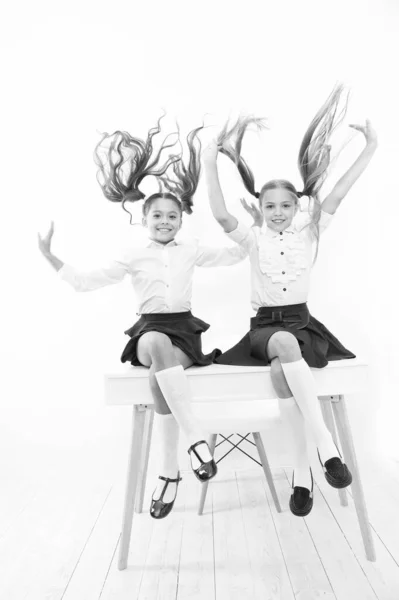 Friskare hår från rot till topp. Bedårande små flickor med flygande hår sitter på skrivbordet. Söta små barn med långt hår ponytails bär skoluniform. Lyxiga hårförlängningar — Stockfoto
