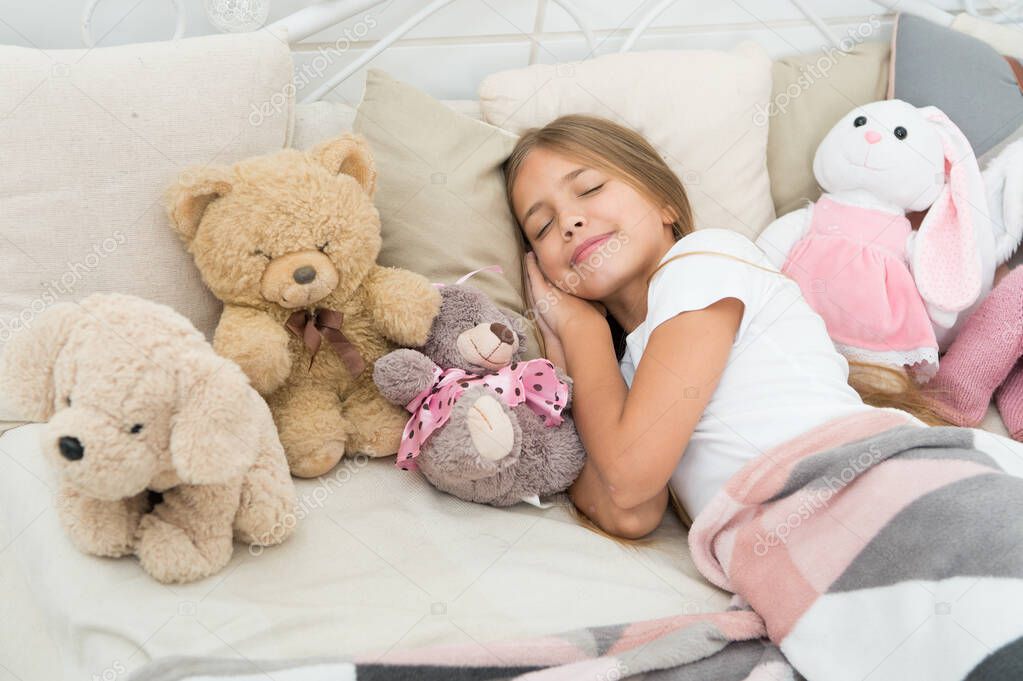 Relaxing before sleep. Girl enjoy evening time with toys. Kid lay bed with toys pillow blanket background. Girl child wear pajamas. Play soft toy before go sleep. Sleep with toy. Carefree childhood