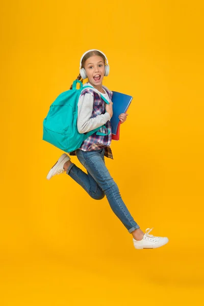 Volviendo a estudiar. Niña enérgica corre al fondo amarillo de la escuela. Niño pequeño con bolso escolar y libros de vuelta a clase. De vuelta a la escuela. Feliz bienvenida de nuevo — Foto de Stock