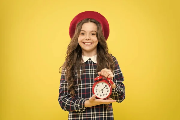 Ketyeg az óra. Kis gyermek mosolyog mechanikus óra sárga háttér. Imádnivaló gyerek hosszú barna hajjal és ébresztőórával. Boldog kislány kezében ébresztőórát — Stock Fotó