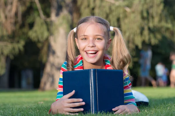 Moja edukacja pochodziła z encyklopedii. Szczęśliwa dziewczynka czyta encyklopedię na zielonej trawie. Uroczy uśmiech małego dziecka z encyklopedią. Encyklopedia i informacje — Zdjęcie stockowe