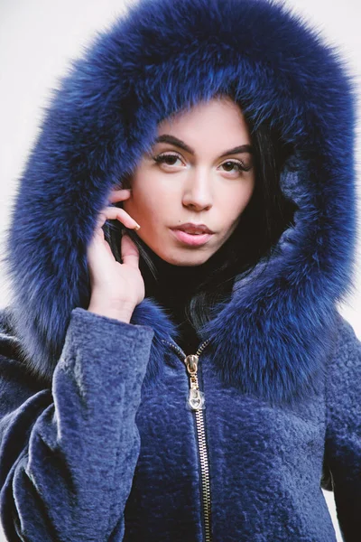 Female with makeup wear dark blue soft fur coat. Woman wear hood with fur. Fashion concept. Girl elegant lady wear fashionable coat jacket with furry hood. Luxurious fur. Girl posing hooded fur coat