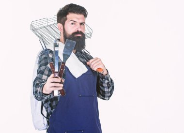 Şehirdeki en iyi barbekü. Izgara aşçı taşınabilir barbekü araçları tutarak. Elinde barbekü ızgarası ve pişirme aletleri olan sakallı adam. Hipster hazırlamak ve barbekü gıda hizmet için metal araçlar kullanarak, kopyalama alanı