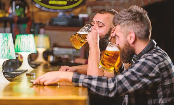 Hipster brutal man drinking beer with friend at bar counter. Men drunk relaxing having fun. Alcohol drinks. Friends relaxing in pub with beer. Refreshing beer concept. Men drinking beer together