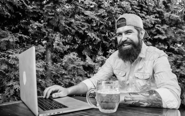Finally friday. Hipster relax sit terrace outdoors with beer. Bearded hipster freelancer enjoy end of working day with beer mug. He deserve this pint. Brutal man leisure with beer and online game
