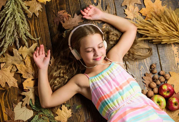 Enjoy perfect sound. Girl lay fallen leaves wooden background. Music application for youth modern gadget. Child girl listen music headphones top view. Autumn music playlist. Enjoy music and relax