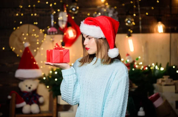 Mysig julstämning. Tro på mirakel. Kvinna jultomte hatt på julafton. Lady bedårande ansikte fira jul hemma. Öppna hennes gåva. Flicka snygg makeup röda läppar hålla jul gåva — Stockfoto