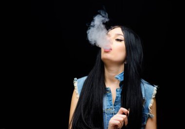 Kız buharı. Göz kamaştırıcı esmer sigara içen siyah arka plan. Dinlen ve rahatla. Nargile barı. Elektronik sigara. Moda kızı vapuru. Beyaz duman bulutu. Vapur kullanmak seksidir. Nikotin bağımlılığı