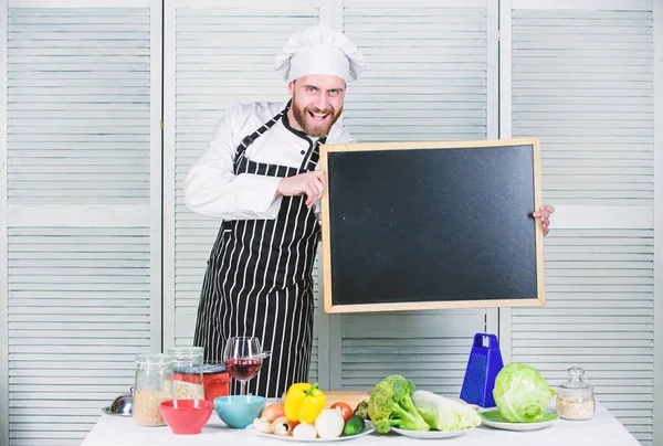 Learning to cook vegetables. Man holding empty blackboard. Chief cook teaching master class in cooking school. Master cook giving cooking class. Education of cooking and food preparation, copy space