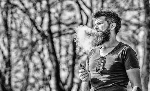 Stress relief concept. Bearded man smoking vape. White clouds of flavored smoke. Smoking electronic cigarette. Man long beard relaxed with smoking habit. Man with beard and mustache breathe out smoke